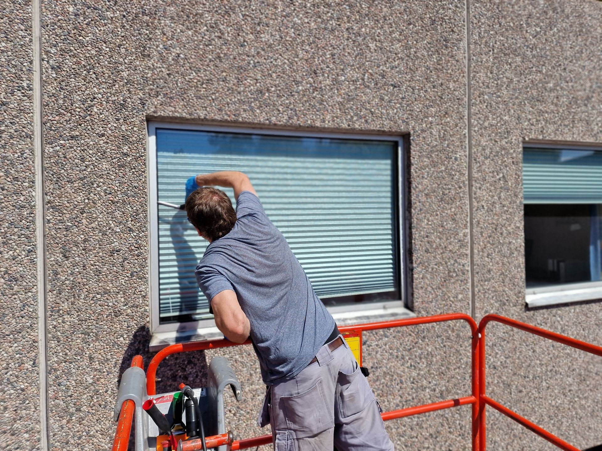 Person cleaning an exterior window of a building using a squeegee while standing on a lift.